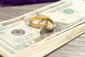 Wedding rings resting on U.S. dollar bills representing financial planning and money conversations for married couples.