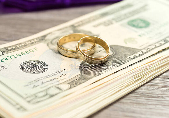 Wedding rings resting on U.S. dollar bills representing financial planning and money conversations for married couples.